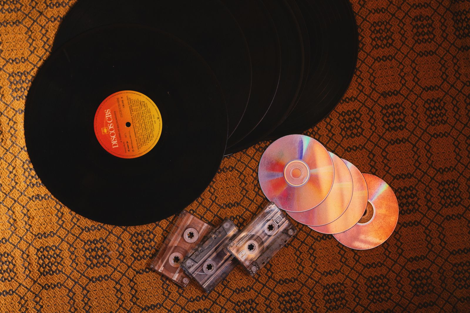Vinylplaten, cd's en cassettes naast elkaar op een kleed