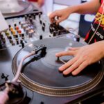 DJ met zijn hand op een plaat op een direct drive draaitafel naast een mixer